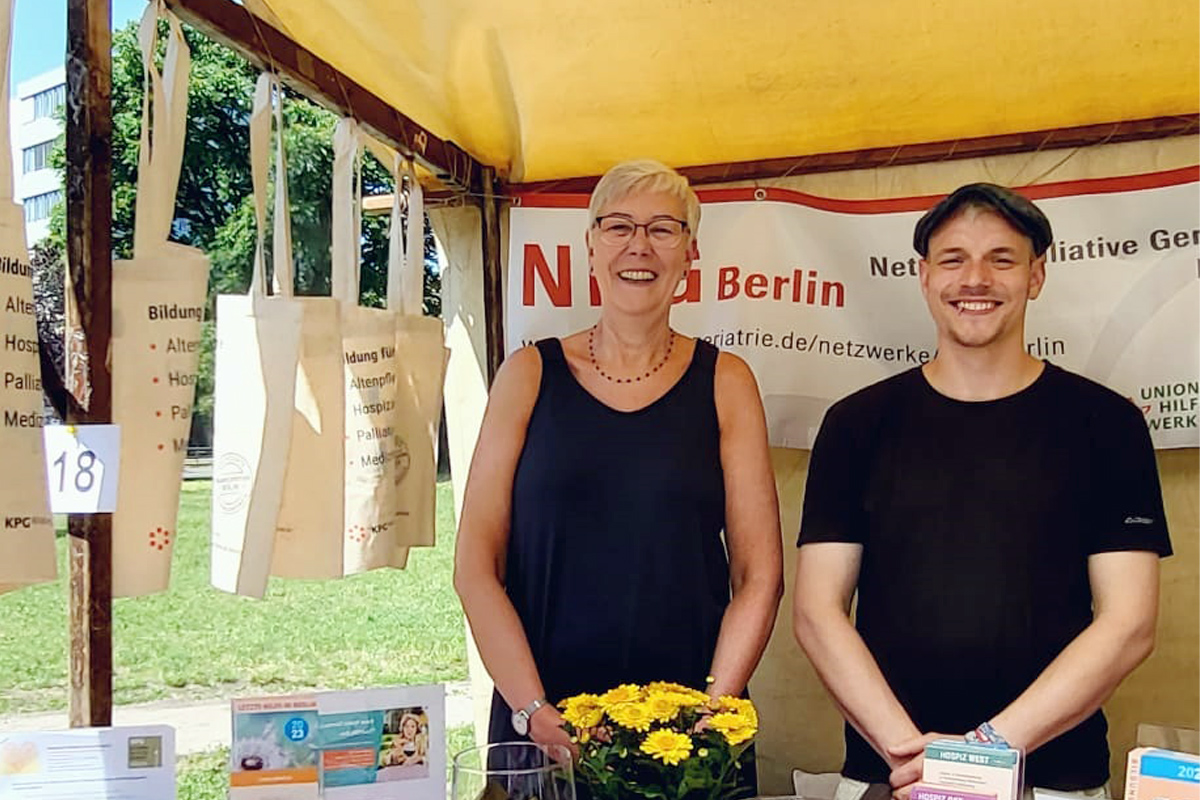 Zwei freundliche Menschen stehen an einem Informationsstand.